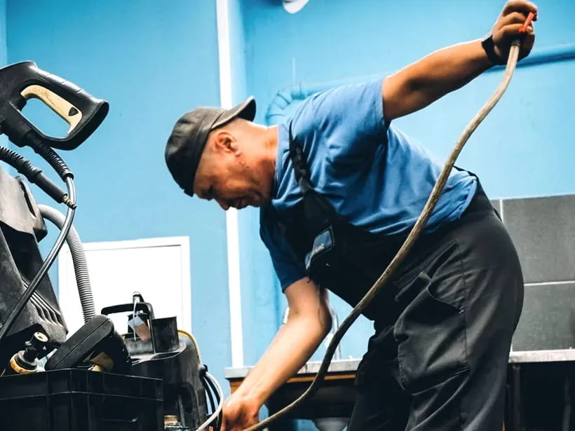 A plumber in a cap and work shirt feeding a drain cable into a line inside a property