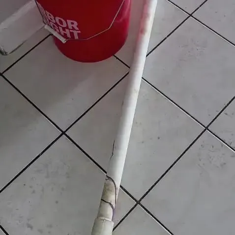 A cracked white PVC pipe running across a tiled floor next to a red work bucket