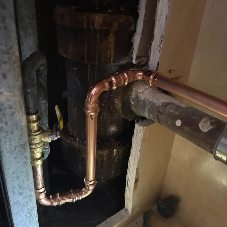 New copper water lines soldered and tied into an existing riser beside a corroded water heater