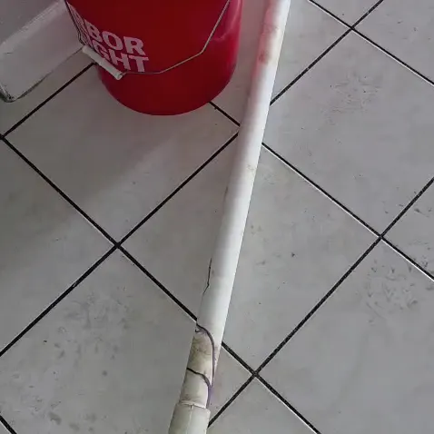 A cracked white PVC drain pipe section removed and laid on a tiled floor
