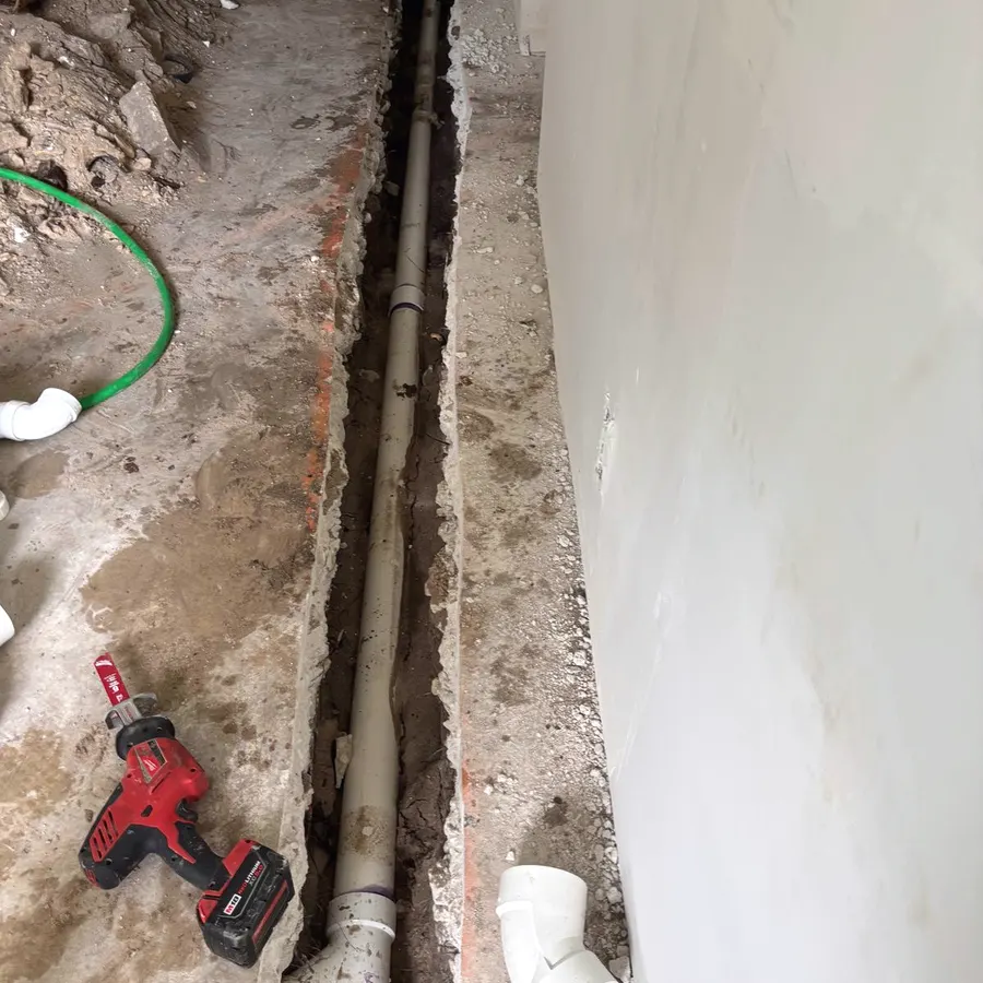Open interior trench cut through a concrete slab with a new PVC drain line laid in it